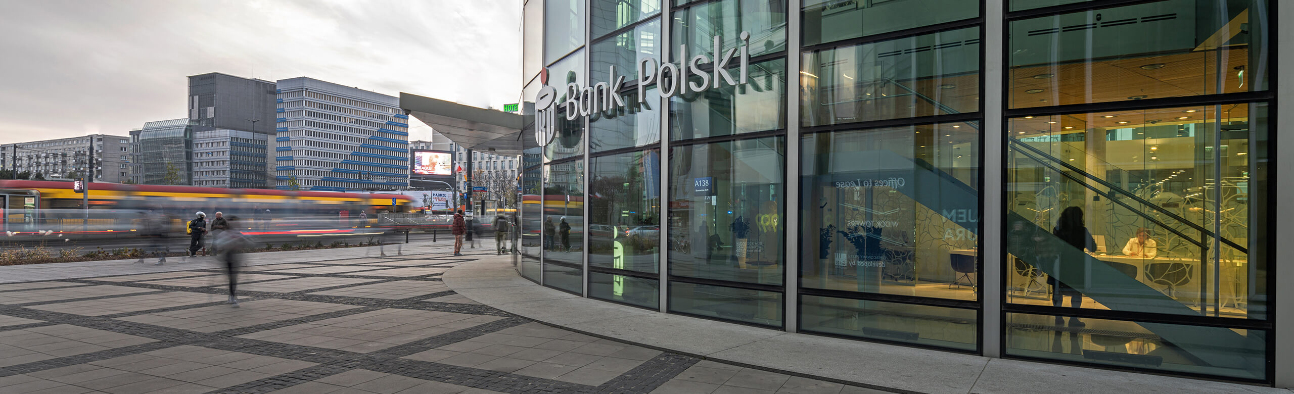 Bank Polski in the Rotunda mixed-use building in Warsaw and other commercial buildings and a tram in the background.